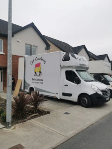 White moving van with Cat Coaching Relocations branding parked on a residential street in front of townhouse-style homes.