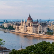 Hungary Budapest Parliament Building with red dome along the Danube River, cityscape on the riverbank and a bridge in the foreground, daytime light.