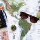 Passport and travel brochures rest on a world map with a pair of sunglasses and colorful pins for planning a trip.