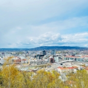 Norway City skyline along a river with low hills in the distance under a partly cloudy blue sky.