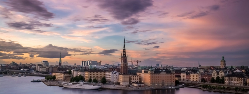 City skyline at sunset with a tall church spire rising above historic buildings along the river.